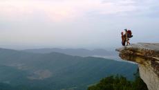 A person stands on McAfee Knob — a piece of land jutting out over a valley with the rolling Blue Ridge Mountains in the background — off the Appalachian Trail