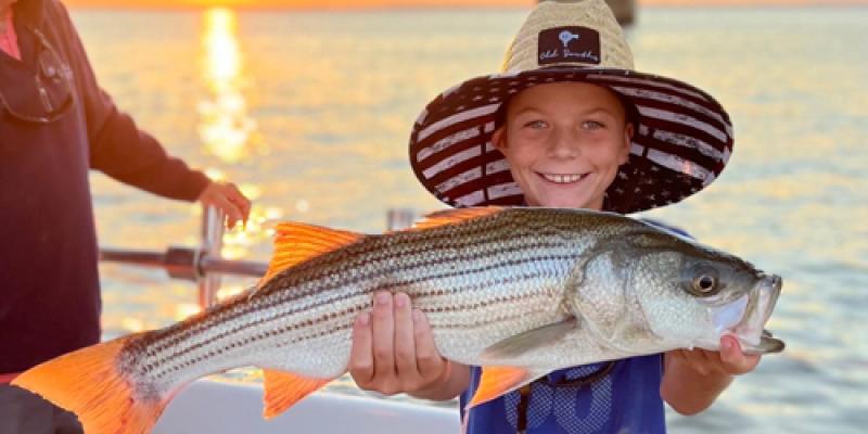 A successful day casting for rockfish on the bay Kid holding a big rockfish with the sun setting over the bay in the background