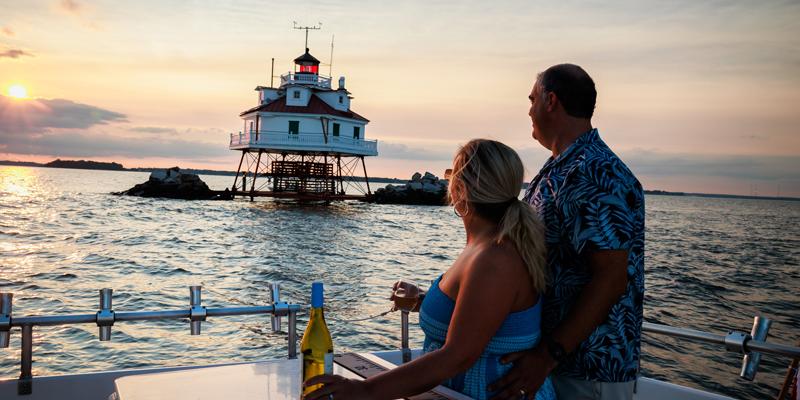 Sunset cruise on the Chesapeake Bay A couple stands on a boat deck with wine admiring a lighthouse on the Chesapeake Bay at sunset