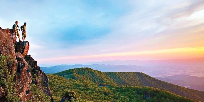 People on a cliff watching the sky turn pink and orange during sunset at Shenandoah National Park in Virginia, USA