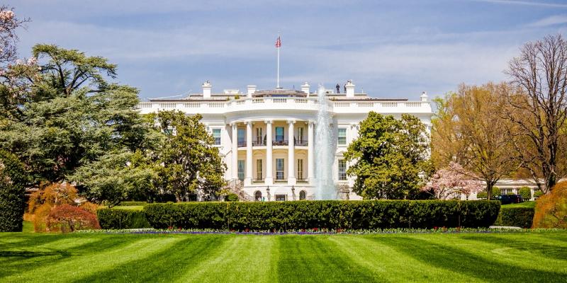 The White House in Washington, DC, USA, in front of a manicured, green lawn on a sunny day.