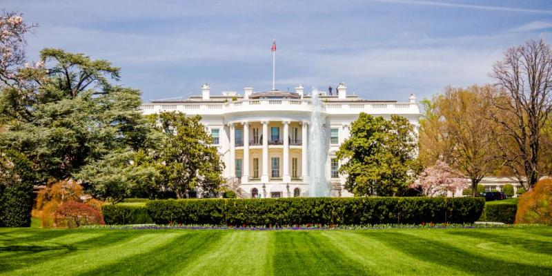 The White House in Washington, DC, USA, in front of a manicured, green lawn on a sunny day.