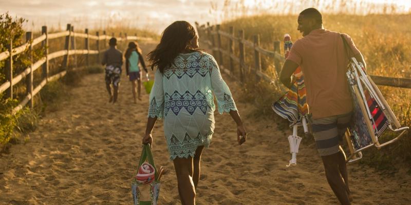 A family of four walks down a sandy path to spend a day on Virginia Beach