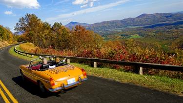 A couple drives a convertible along the parkway in autumn