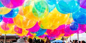 A cloud of colorful balloons hangs above a crowd