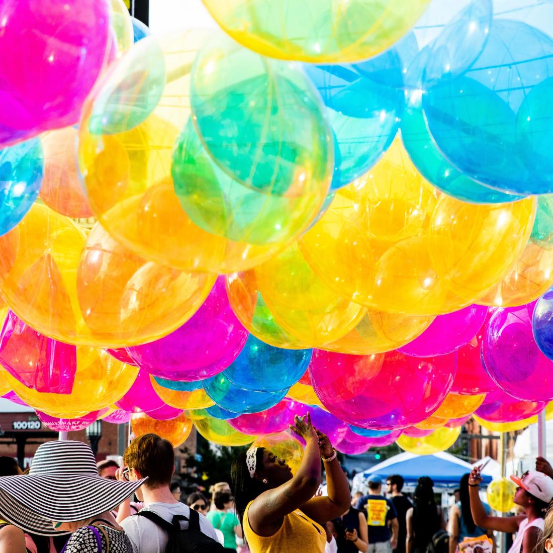 A cloud of colorful balloons hangs above a crowd